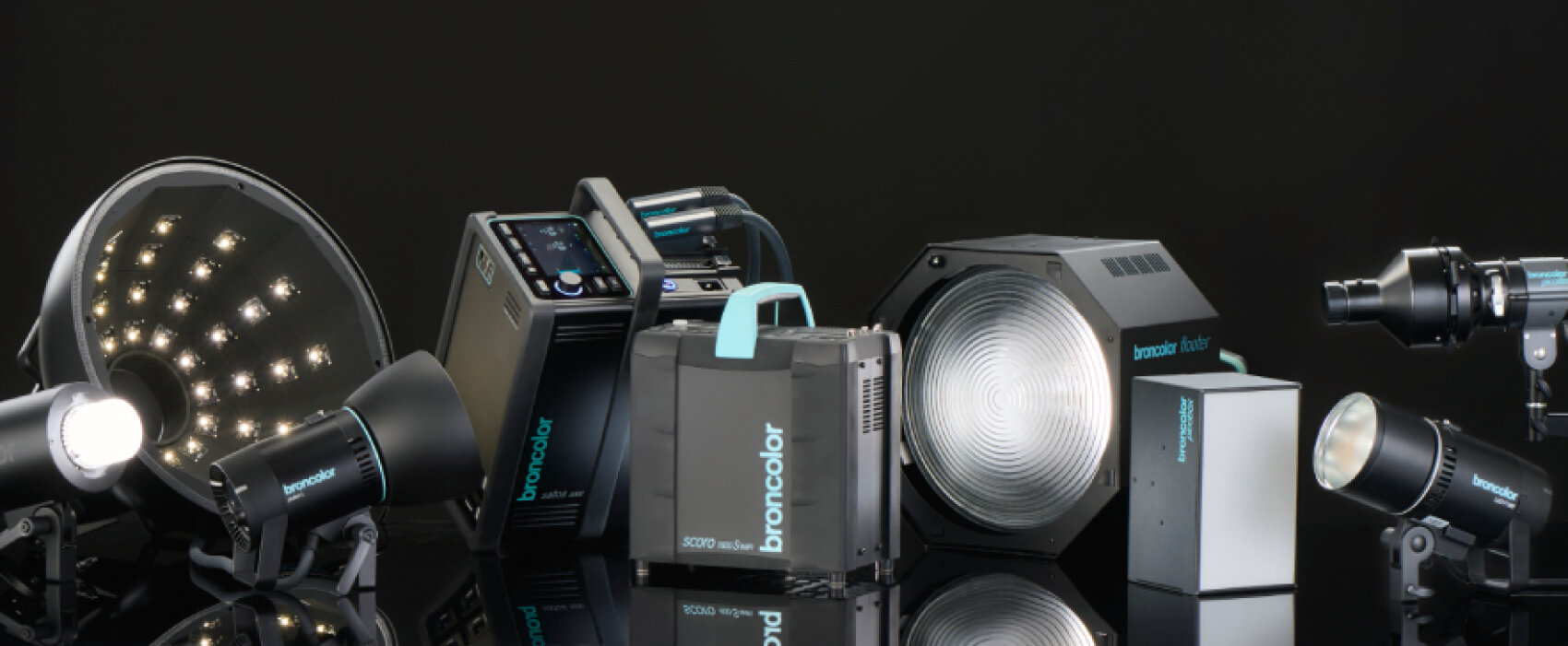 Une collection d'équipements professionnels d'éclairage de studio Broncolor, comprenant des lampes LED, des boîtes à lumière et des blocs d'alimentation, disposés sur une surface noire réfléchissante avec un arrière-plan sombre.